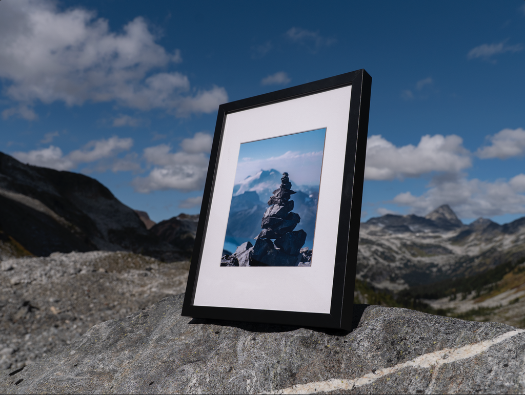 Angled view of the black-framed Heights print on a rock beneath a blue sky.